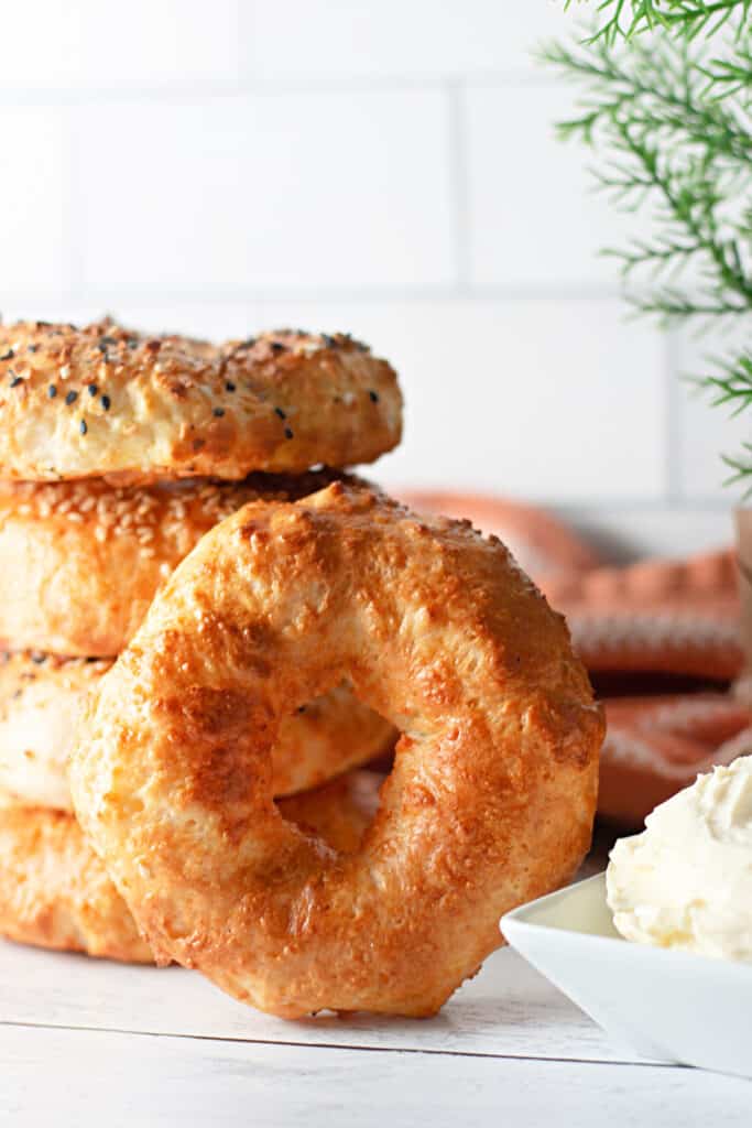 Stacked air fryer bagels on a white kitchen countertop, bowl of cream cheese spread.
