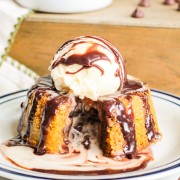 Pumpkin lava cake with a scoop of vanilla ice cream on top on a white serving plate, melted chocolate ganache oozing from the center of the pumpkin lava cake.