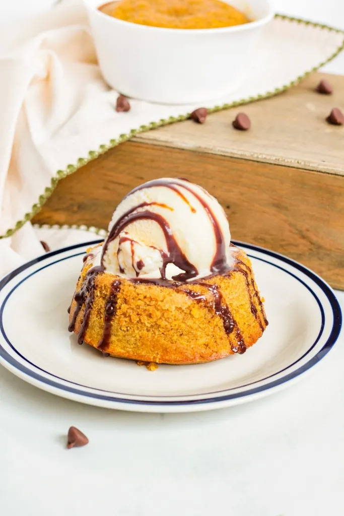 Pumpkin lava cake on a plate with a scoop of vanilla ice cream on top, om a white countertop, pumpkin puree in the background.