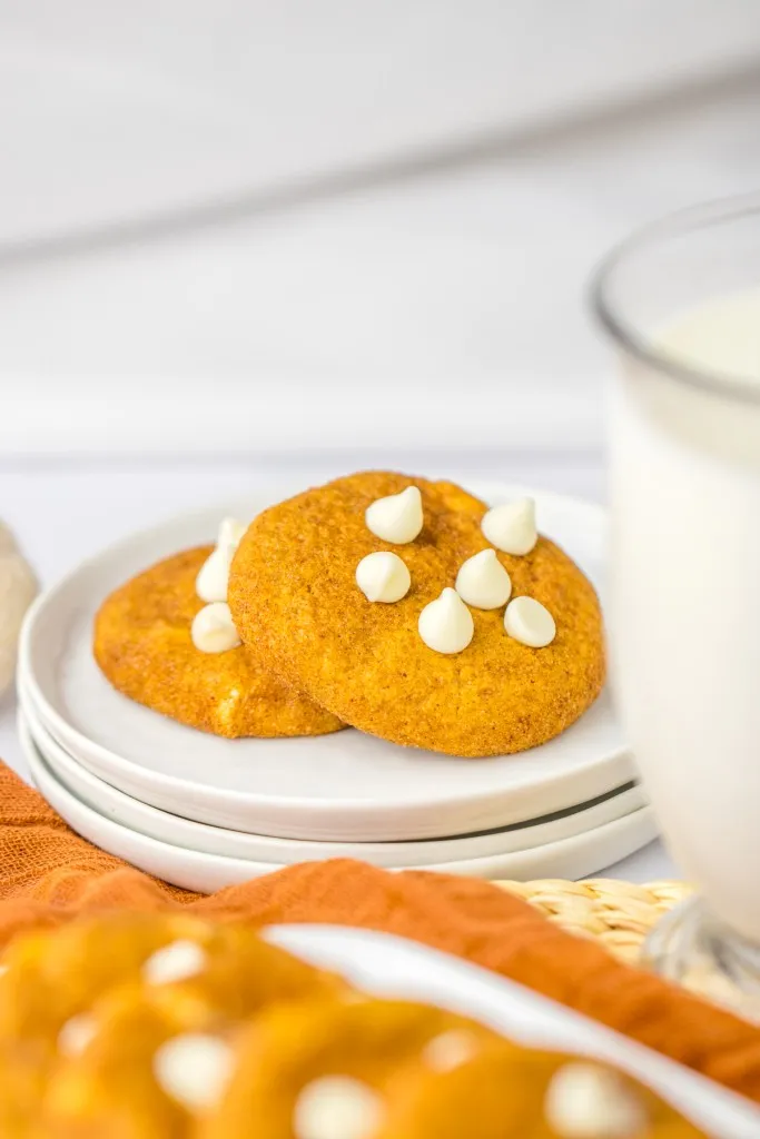 White stacked plates with pumpkin snickerdoodle cookies, glass of milk, tray of pumpkin snickerdoodle cookies.