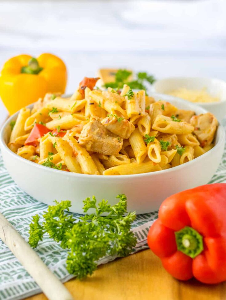 Bowl of slow cooker Cajun chicken pasta with fresh bell peppers and parsley on a countertop.