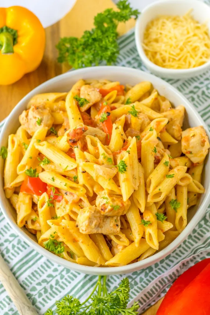 Overhead view of a bowl of slow cooker Cajun chicken pasta with fresh bell peppers and parsley on a countertop.