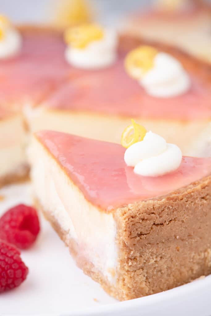 Close up of sliced lemon raspberry cheesecake on a white plate with fresh loose raspberries.