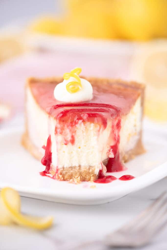 Close up of a single slice of lemon raspberry cheesecake with a forkful removed.