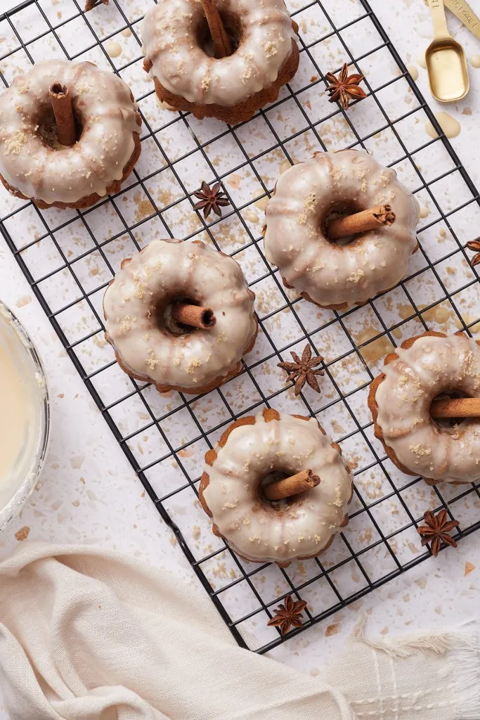 Overhead view of mini pumpkin bundt cakes on a wire rack, cream cloth on a white marble countertop.