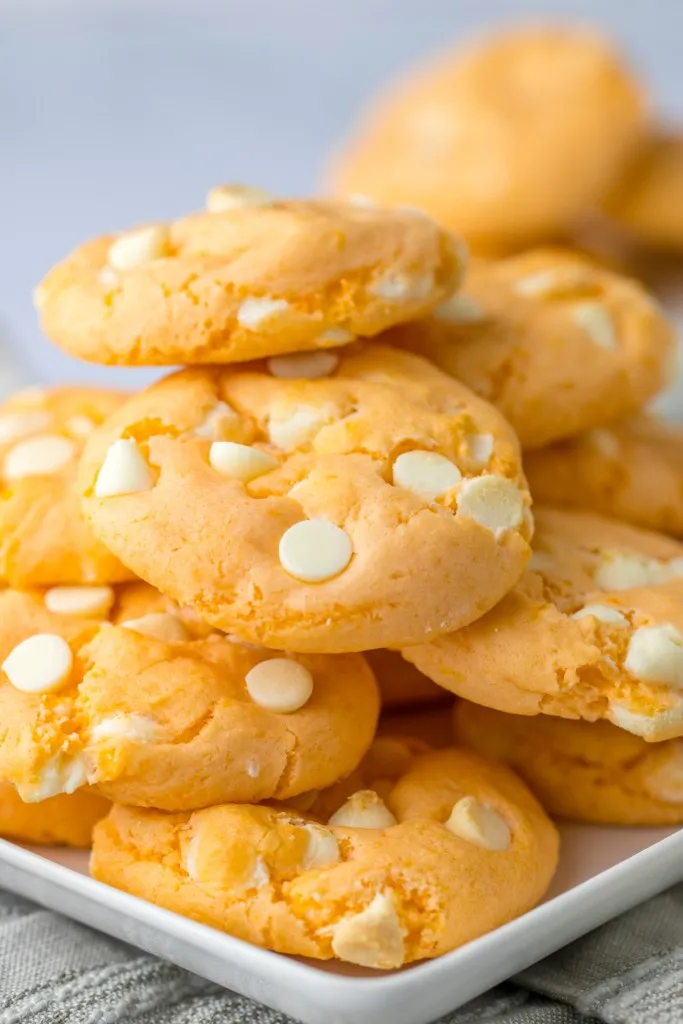 Close up of piled orange creamsicle cookies on a white plate.