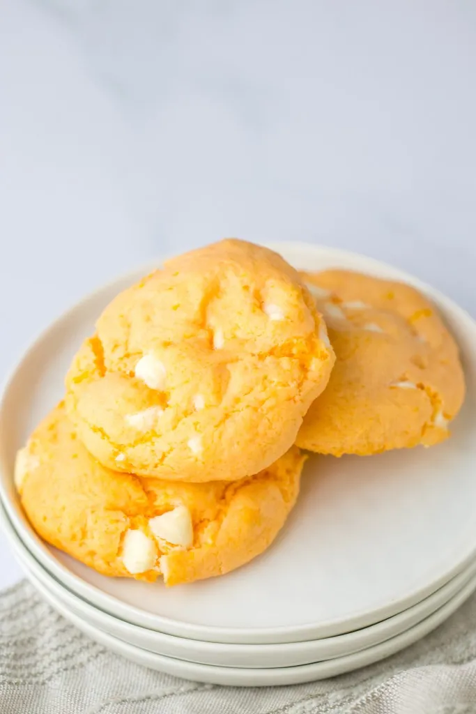 Three orange creamsicle cookies on white stacked plates, neutral cloth on a white marble countertop.