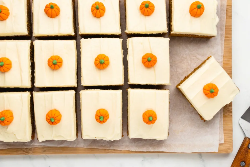 Overhead view of pumpkin cake with cream cheese frosting on a wooden board lined with parchment paper.