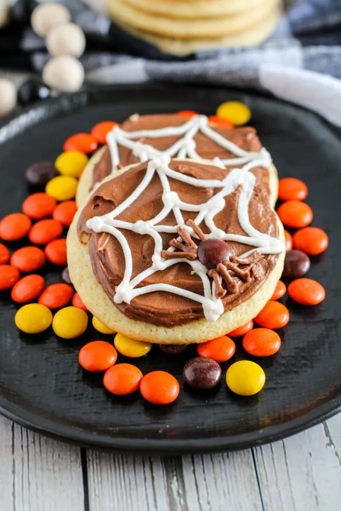 Close up of easy spider web sugar cookies on a black plate with Reese's pieces.