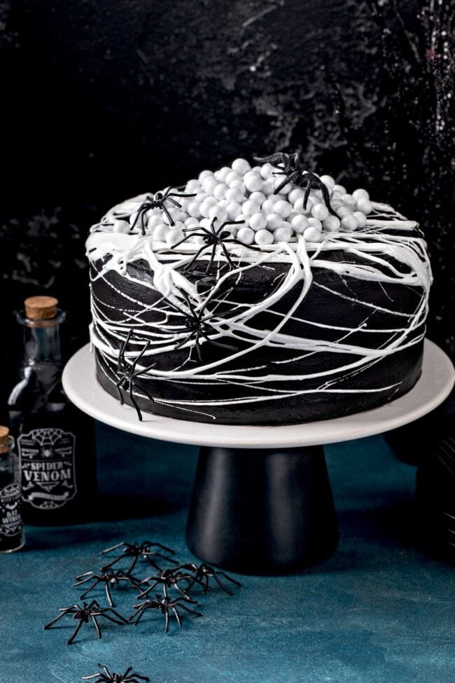 black cake with white frosting in shapes of spider webs with crawling spiders