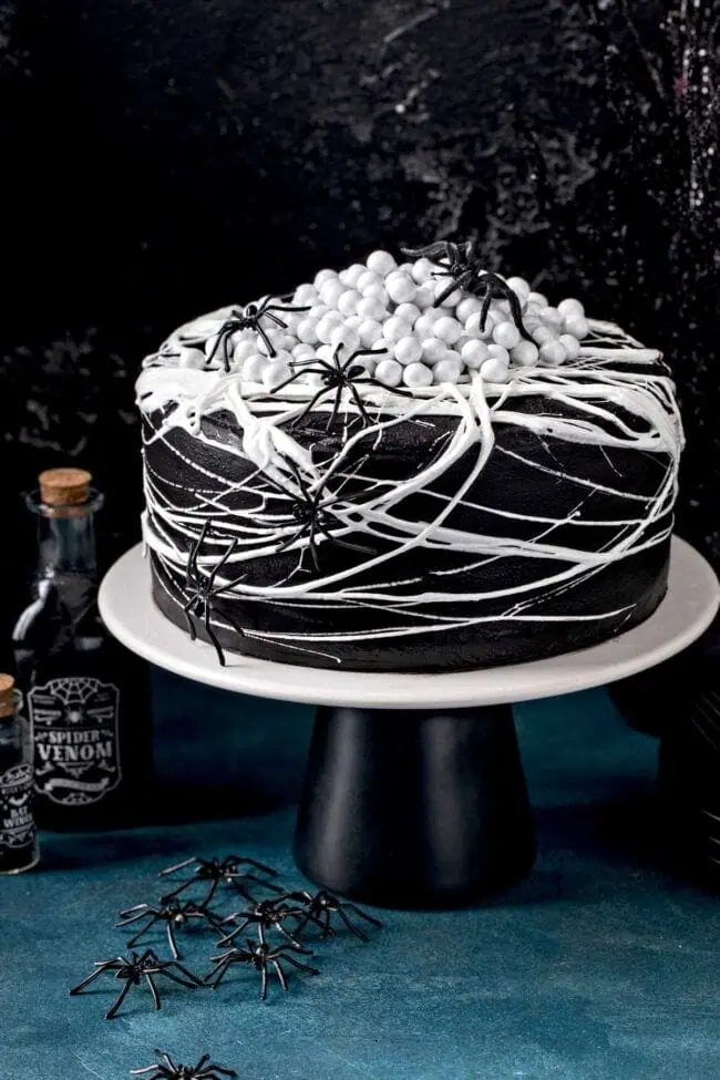black cake with white frosting in shapes of spider webs with crawling spiders
