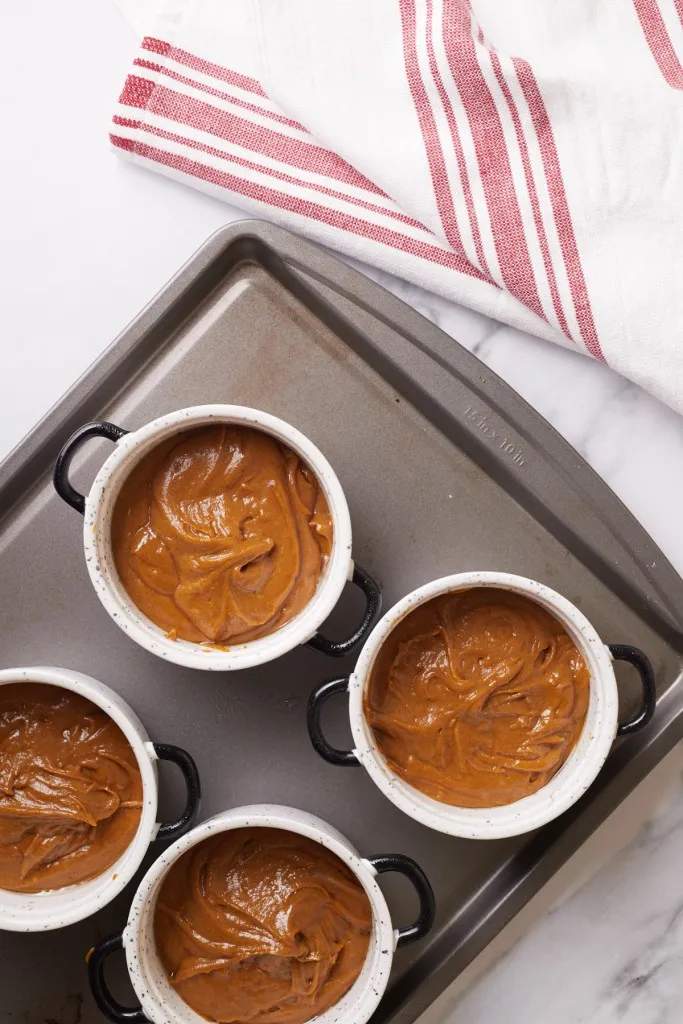Ramekins on a baking sheet filled with gingerbread pudding cake batter.