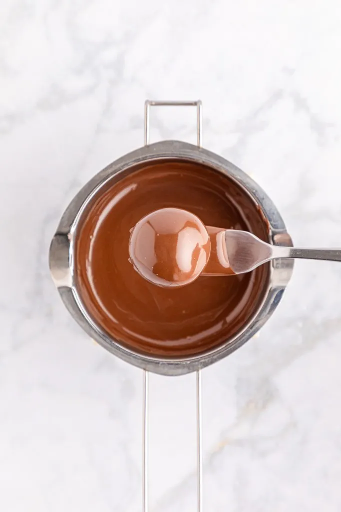 Double boiler with melted dark chocolate wafers, Oreo ball on a fork coated in the melted chocolate.