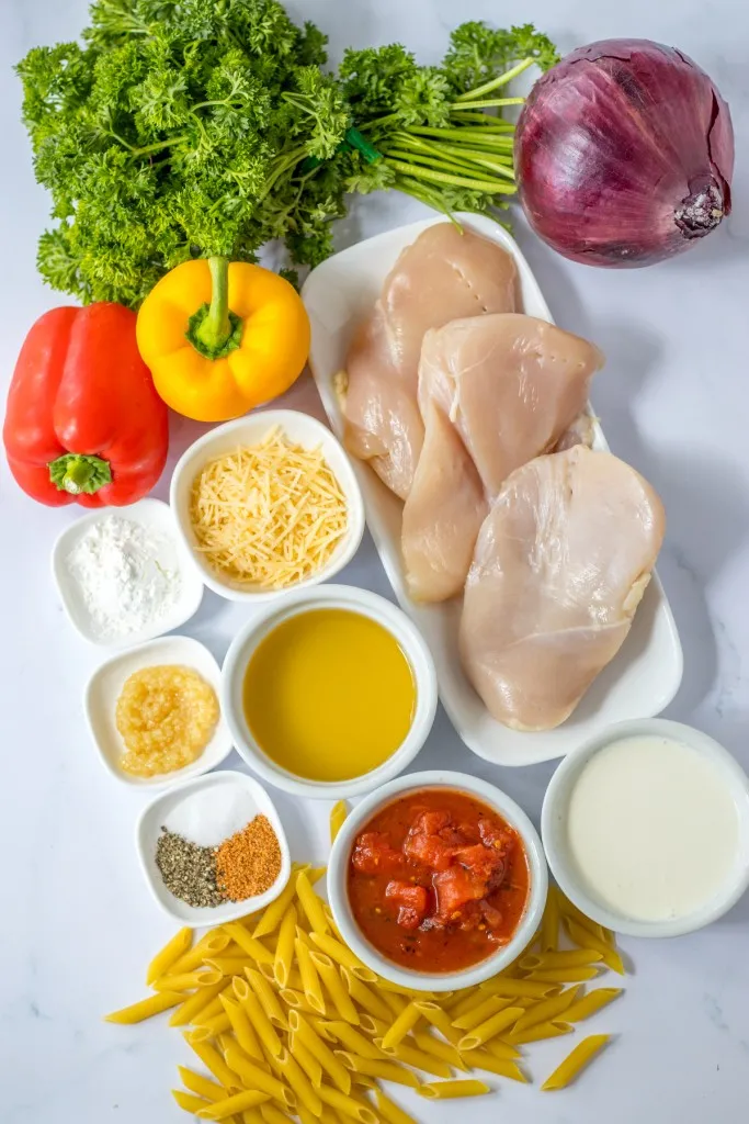 Ingredients for slow cooker Cajun chicken pasta on a marble countertop.