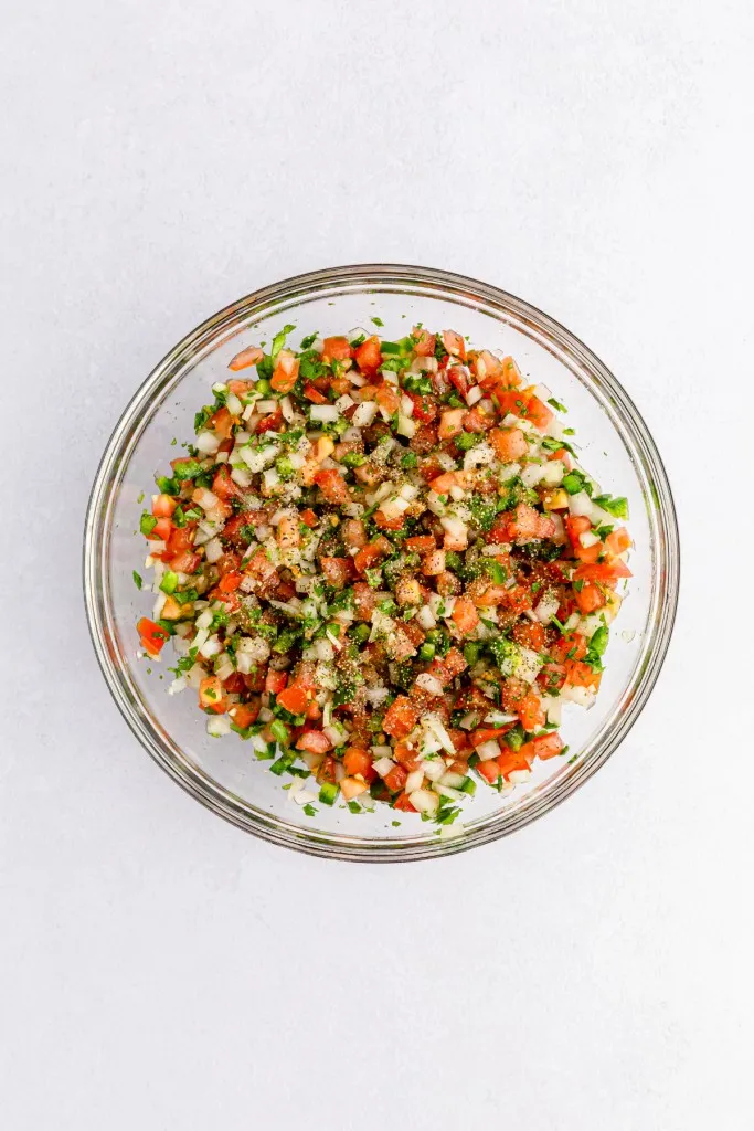 Pico de Gallo ingredients in a mixing bowl with seasoning added.