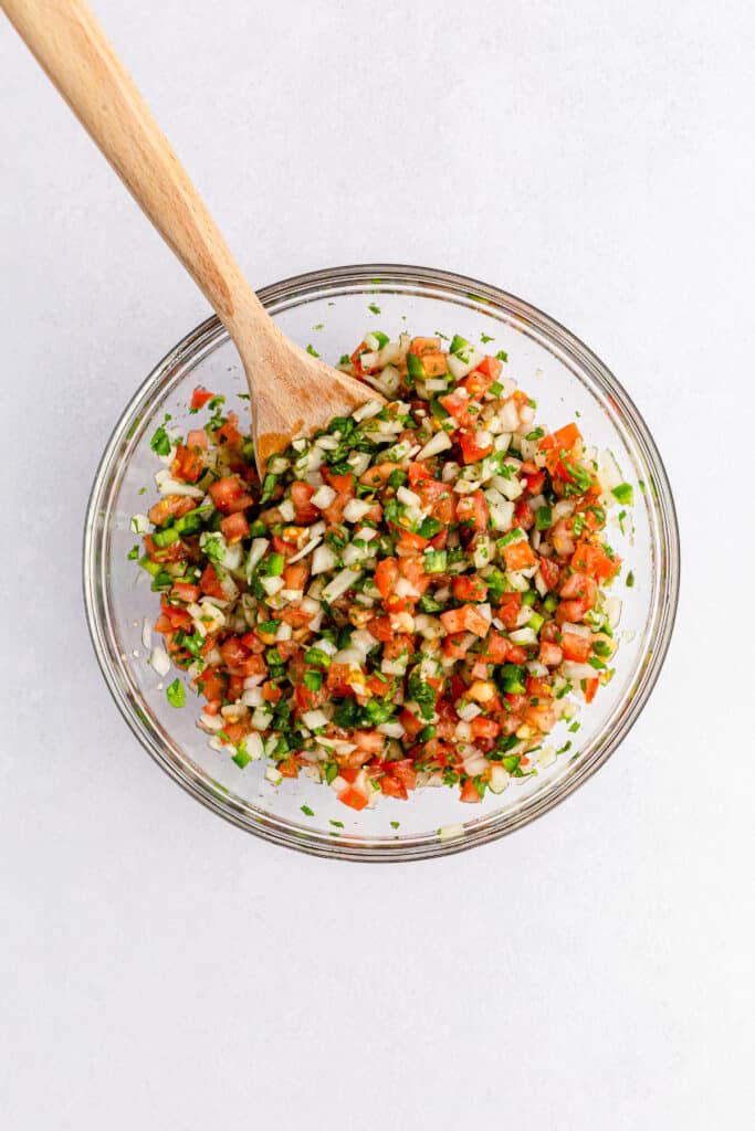 Pico de Gallo ingredients in a medium mixing bowl with a wooden spoon. 