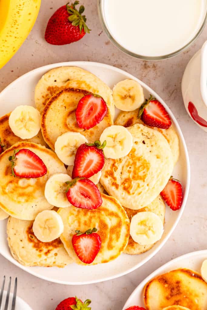 a close up view of mini pancakes garnished with sliced bananas and strawberries off to the side