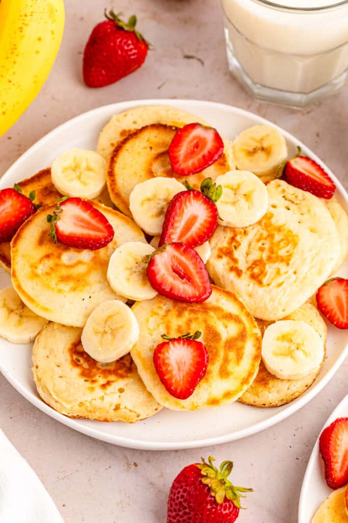 a close up view of mini pancakes garnished with sliced bananas and strawberries