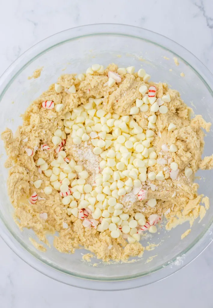 Mixing bowl with white chocolate and peppermint cookie dough, white chocolate chips, and crushed peppermints.