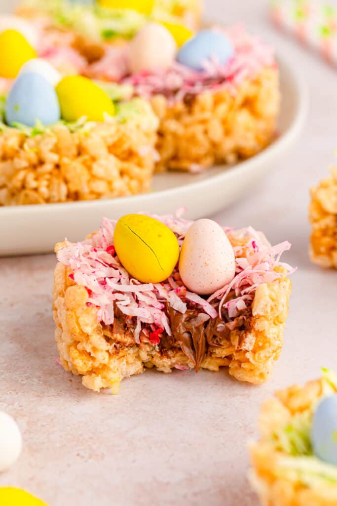 side view of easter rice krispies nests with green and pink coconut grass witha bite taken out of it