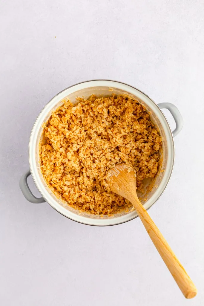 Large pot with Rice Krispies cereal coated in melted butter and mini marshmallows with a wooden spoon.