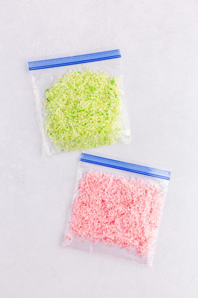 Two Ziploc bags with thin coconut shreds and gel food coloring being rubbed onto the shreds. 