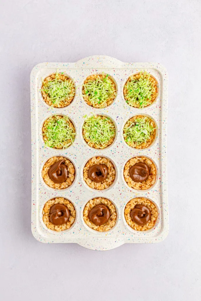 Mini muffin tray with Rice Krispies Nests, Nutella centers, and topped with colored coconut shreds.
