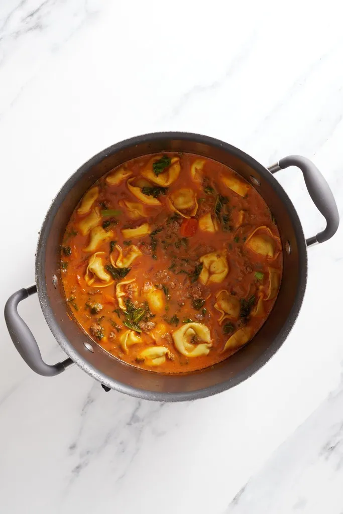 Overhead view of sausage kale tortellini soup mixture in a pot.