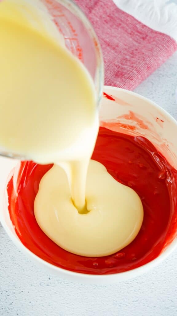 Mixing bowl with melted red candy melts, heated buttercream being poured into the red candy melt mixture.