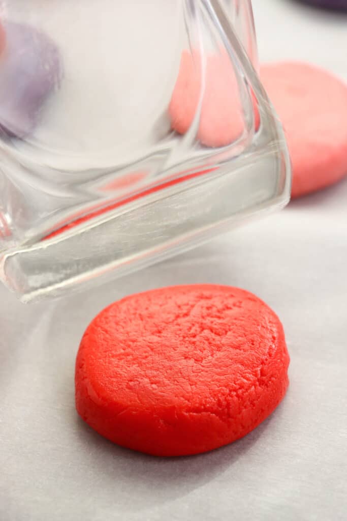 Single Valentine's whoopie pie dough ball flattened by the back of a drinking glass on a baking sheet.