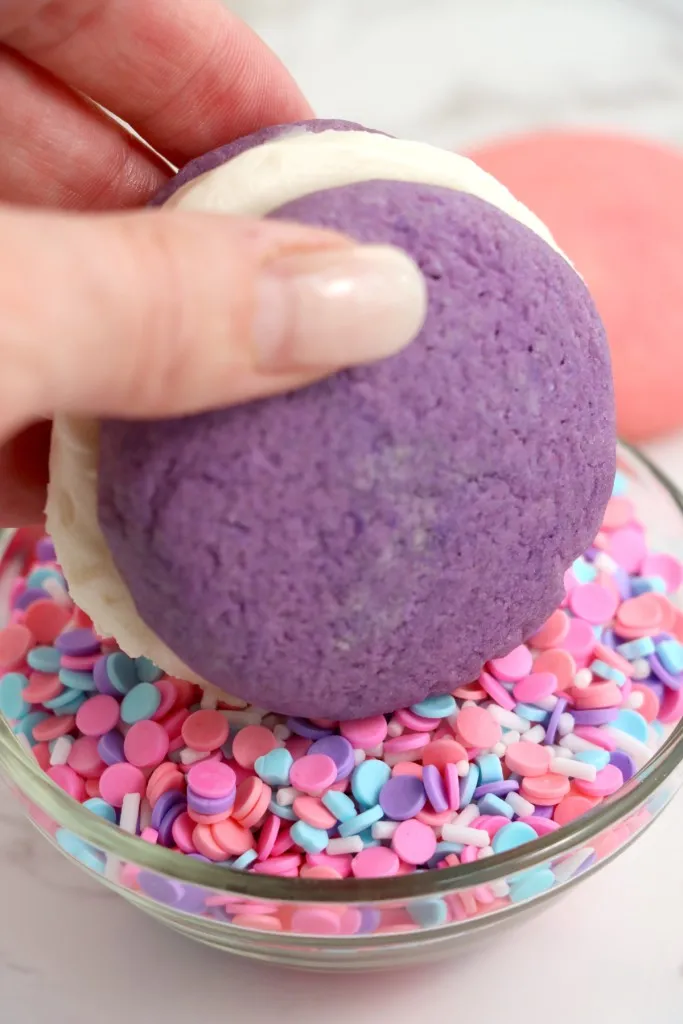 Assembled Valentine's whoopie pie rolled in a small bowl of colored sprinkles.