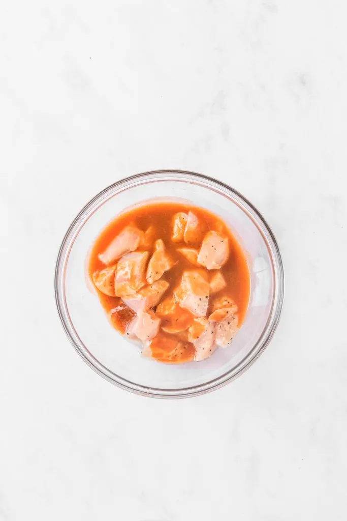 Mixing bowl with chicken pieces in melted butter, hot sauce, and seasoning. 