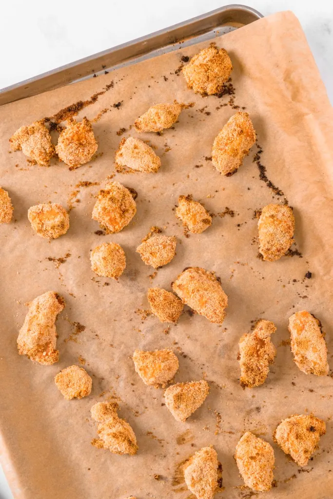 Baked breaded chicken pieces on a parchment-lined baking tray. 