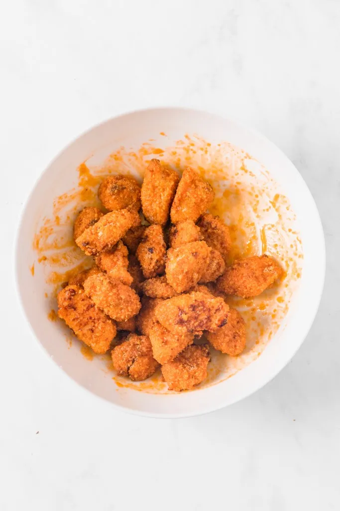 Baked and breaded chicken pieces in a bowl, mixed with extra hot sauce.