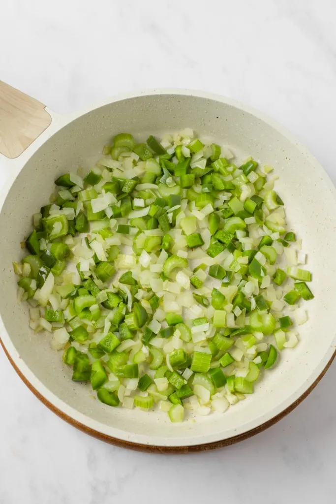 Large skillet with diced onion, green bell pepper, and celery. 