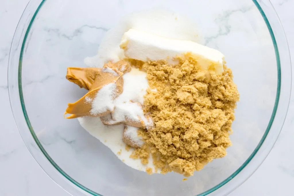 A large mixing bowl with white and brown sugar, peanut butter, and softened butter.