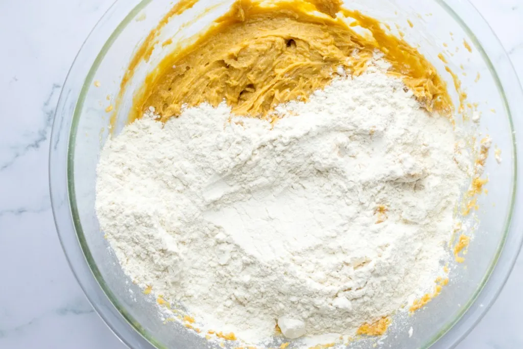 Large mixing bowl with cookie dough, flour, baking soda, and baking powder. 