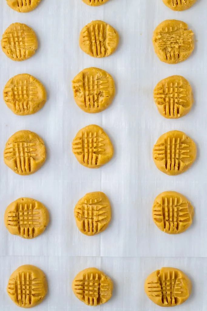 Overhead view of slightly flattened peanut butter cookie balls with criss-cross patterns on the top. 