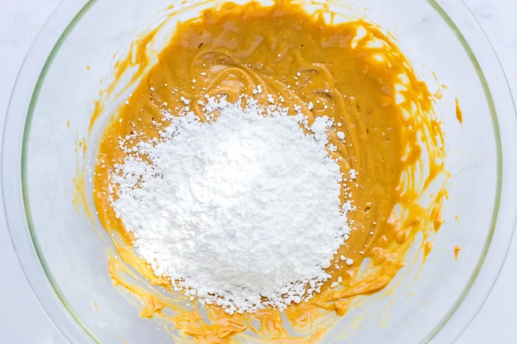 Mixing bowl with mixed peanut butter and softened butter, with powdered sugar added. 