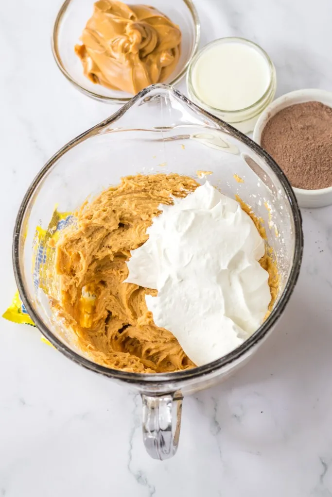 Glass mixing bowl with peanut butter, cream cheese, powdered sugar, and 2 cups of whipped cream folded into the mixture.