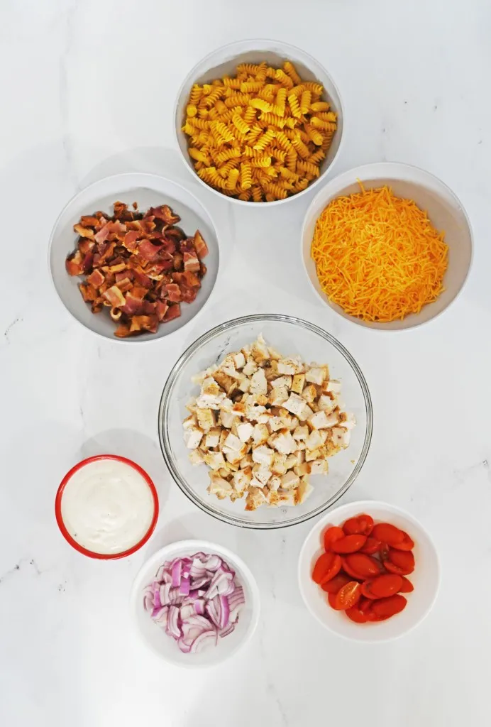 Ingredients for Chicken Bacon Ranch Pasta Salad on a marble countertop.