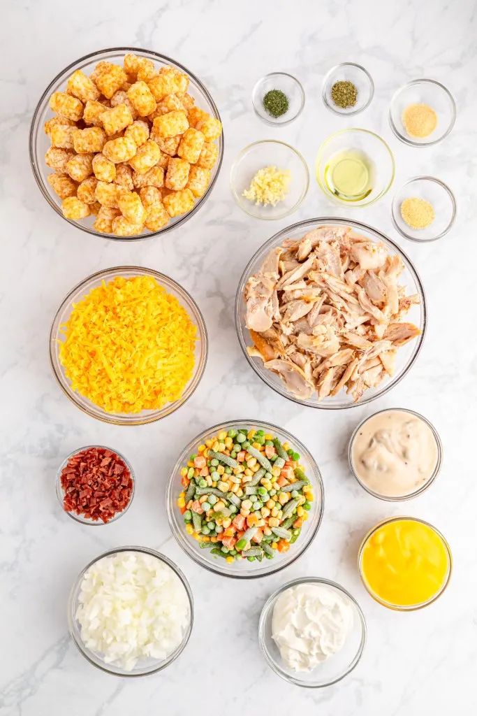 Chicken tater tot casserole ingredients in separate bowls on a marble countertop.