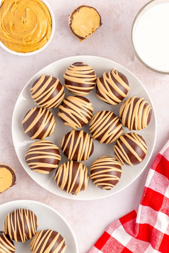 Overhead view of two plate loaded with chocolate covered peanut butter balls, recipe ingredients placed around the serving plates, red and white checkered cloth to the side.