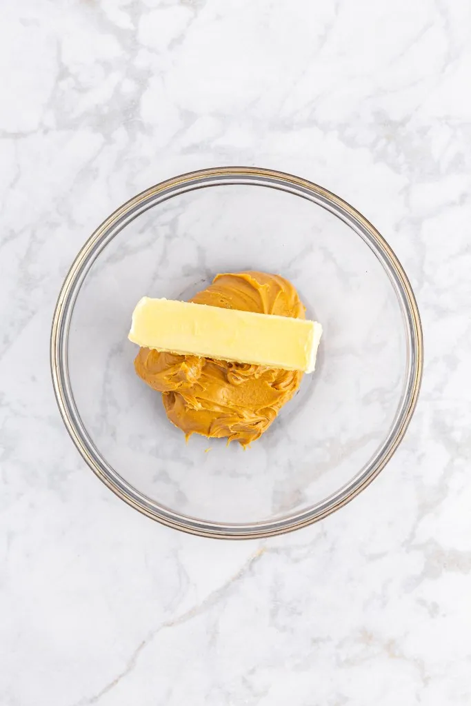 Large glass mixing bowl with creamy peanut butter and unsalted butter.