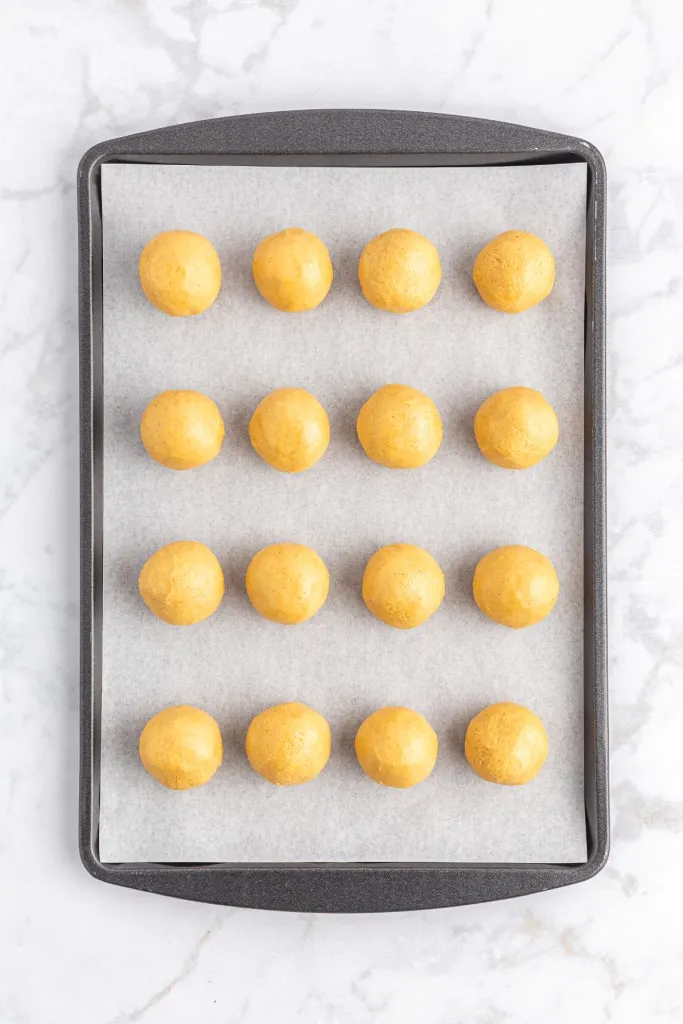 Parchment-lined baking tray with rolled peanut butter balls.