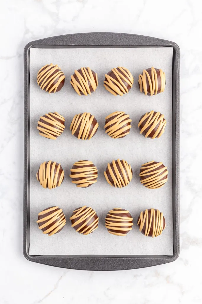 Parchment-lined baking tray with chocolate covered peanut butter balls with peanut butter drizzle.