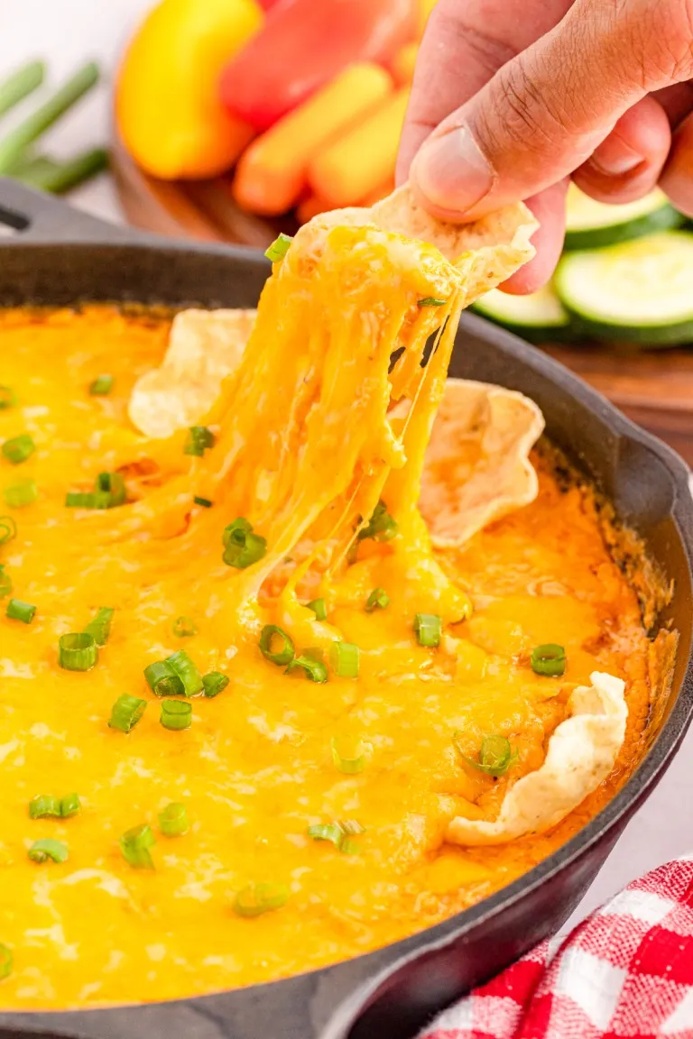 Fingers holding a tortilla chip and dipping it into the skillet filled with baked buffalo chicken dip.