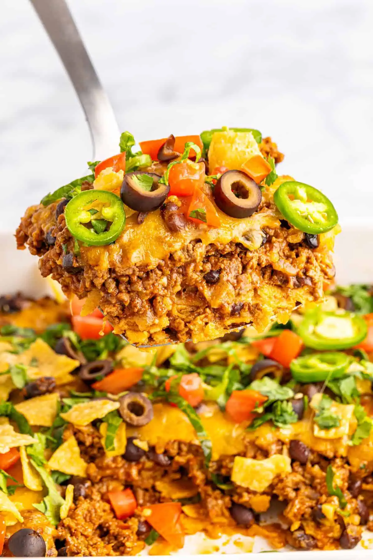 Close up of a serving of easy taco casserole lifted out of a white casserole dish by a silver server.