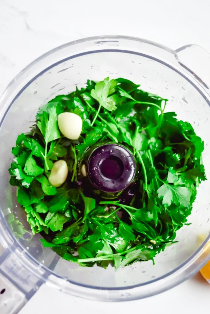 Garlic cloves added to a food processor with parsley and lemon juice.