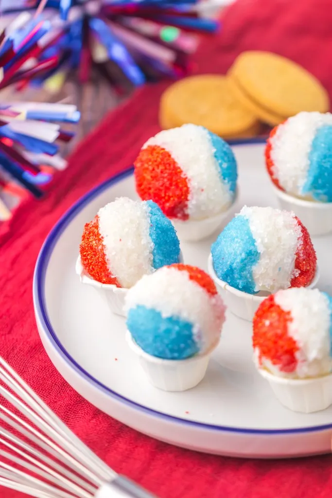 Snow cone Oreo truffles on a serving plate with 4th of July-themed decorations in the background.